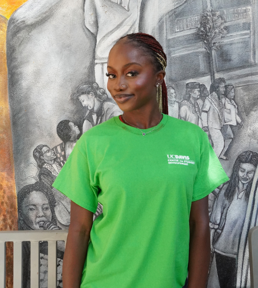 Young Black woman in green T-shirt standing before a grayscale mural
